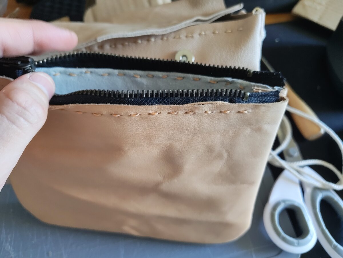 Pochette en cuir naturel beige avec fermeture éclair bleue, tenue en main